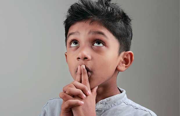 young boy looking up with hands in thinking position over mouth