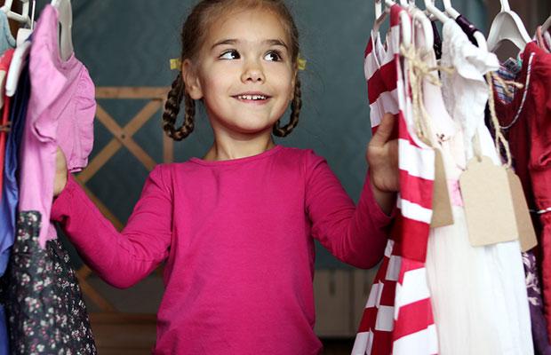 girl child looking at dresses hanging in a closet