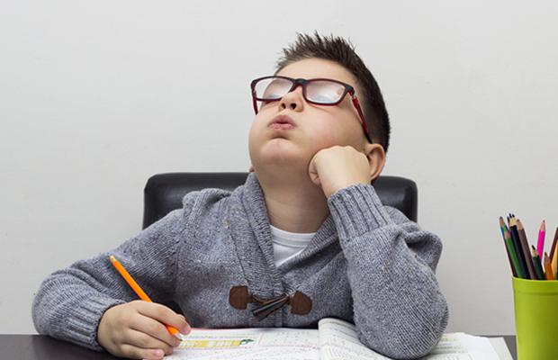 young boy doing schoolwork, head back, cheeks rounded, and mouth blowing out air