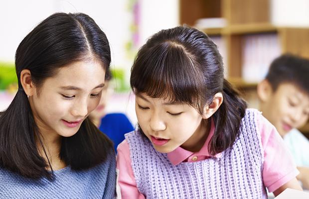two young girls with heads together talking and looking down at something