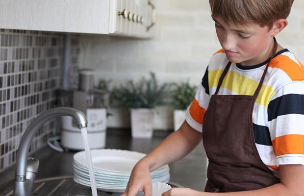 teen boy wearing an apron and doing the dishes