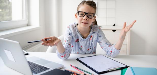 girl in glasses doing schoolwork in her pajamas, elbows on table and hands splayed out